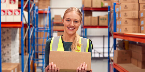 Portrait Of Female Worker Holding Box Inside Warehouse